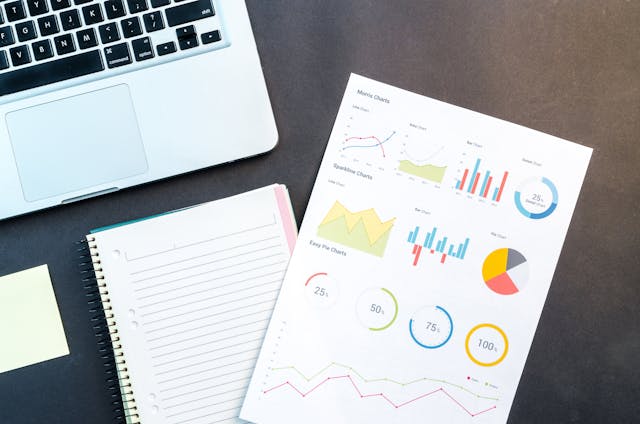 A paper with colored graphs and charts next to a laptop and notebook.
