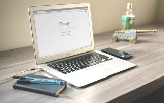 A laptop next to a notebook with Google on the screen.